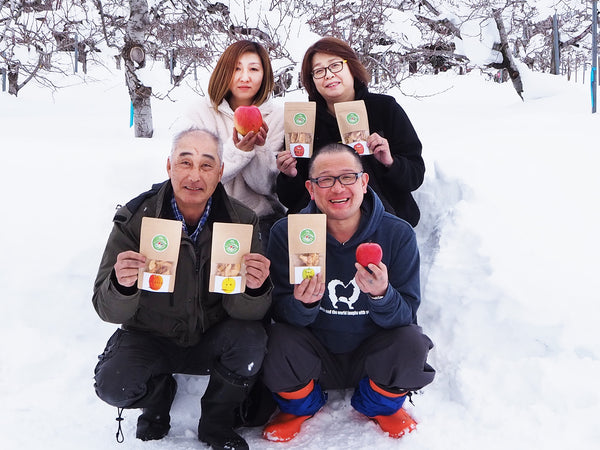 ドライフルーツのパッケージを手に雪の中にしゃがむすこやか自然農園の4名の男女